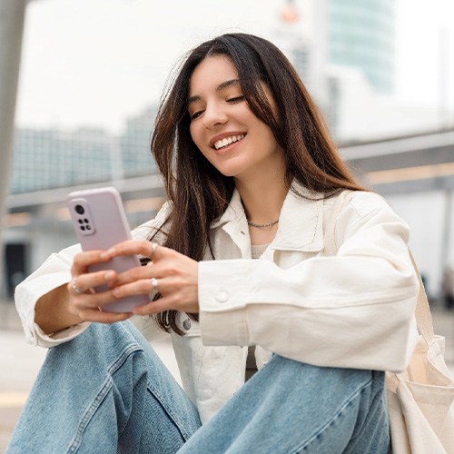 Teen girl smiling while looking at phone outside