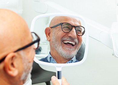 Man with glasses smiling at reflection in handheld mirror