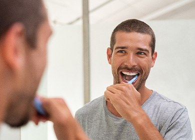 Patient brushing dental implants at bathroom sink 