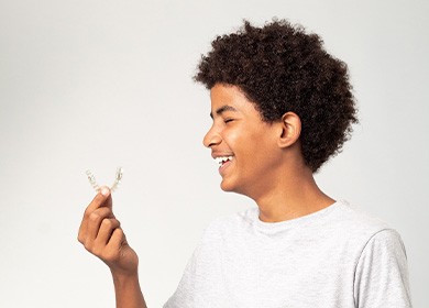 Teenage boy smiling while holding clear aligner