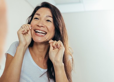 Woman smiling while flossing in bathroom
