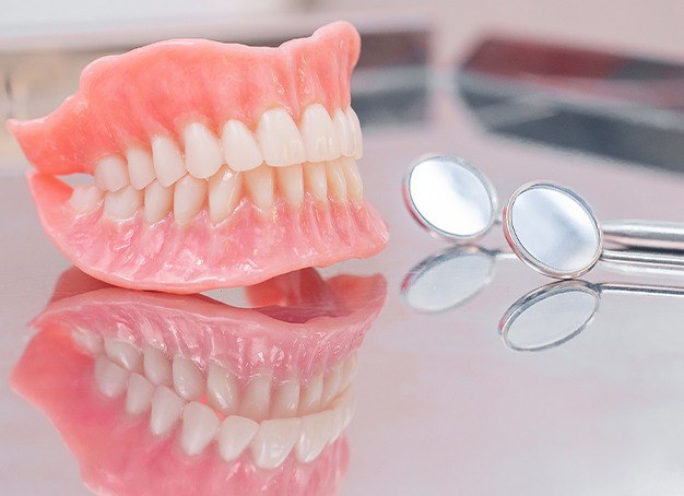 Full set of dentures and dental treatment tools on reflective surface