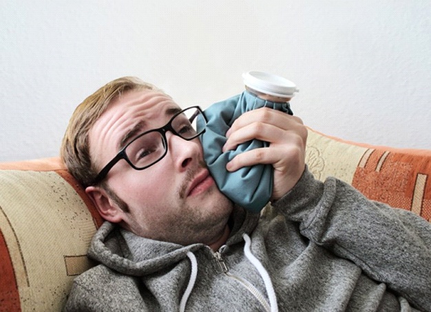 man lying on a couch and holding a cold compress to his cheek