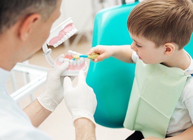 Kid friendly dentist teaching child to brush teeth