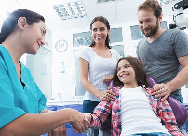 Child in dental office with her parents smiling at dentist