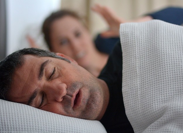 Man in need of sleep apnea therapy snoring in bed next to frustrated partner