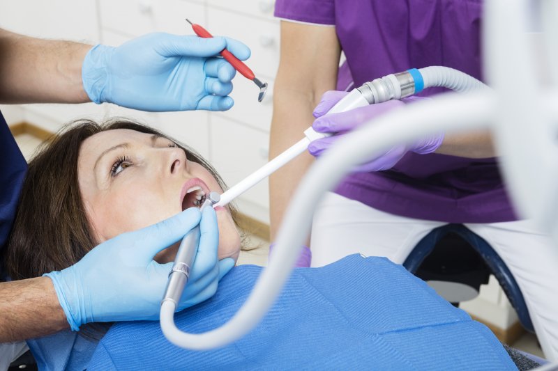 a female patient lying back in a dentist’s chair while a dental assistant administers chairside suction