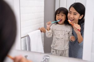 a parent and their child brushing their teeth together to maintain good oral health