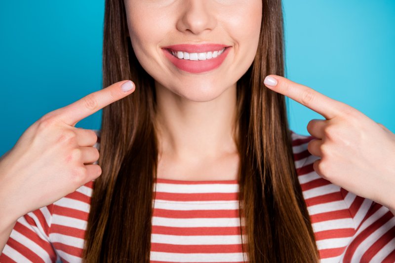an up-close view of a woman pointing to her smile after receiving cosmetic dentistry