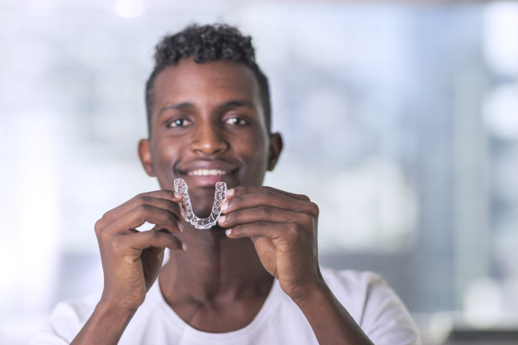 person smiling while holding Invisalign aligner