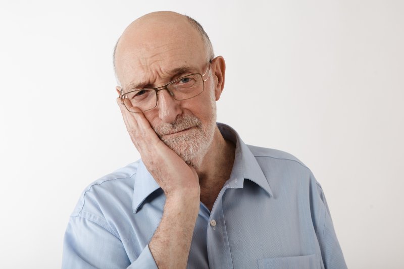 Older man holding his cheek because of denture sores