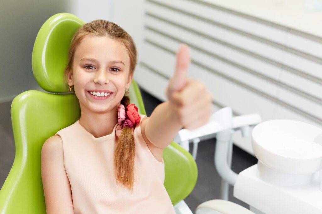 child sitting in dental chair smiling and giving thumbs up