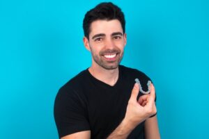 Man smiling and holding up his clear aligners